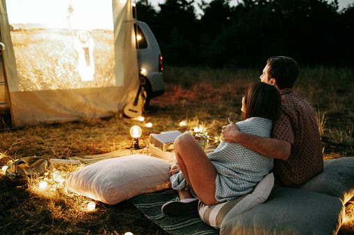 Jeune couple assis devant une voiture lors d’une séance de cinéma en plein air, illustrant une rencontre sérieuse, la communication et les premiers moments d’une relation durable.