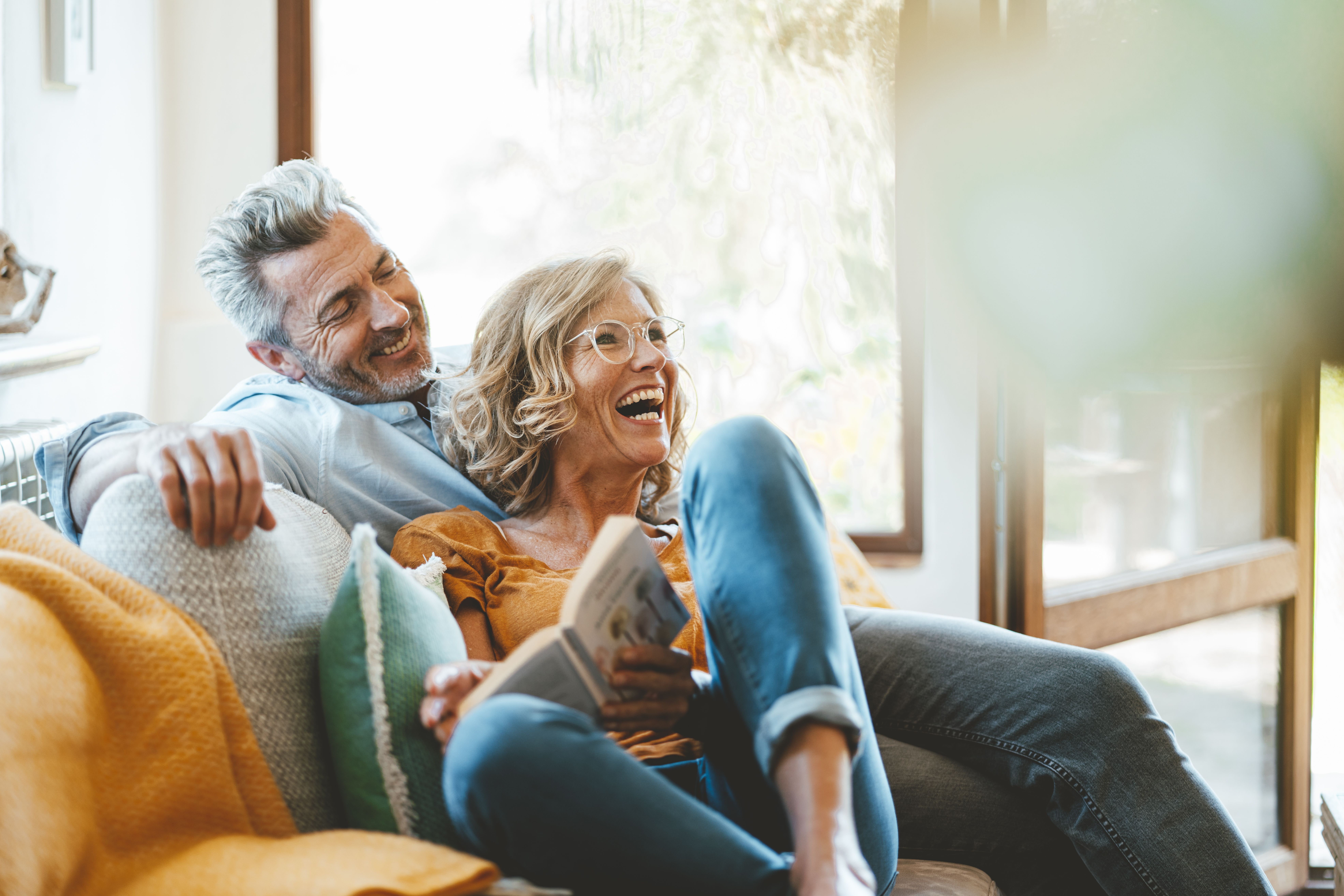 Couple d’une quarantaine d’années souriant sur un canapé à la maison, partageant un moment de complicité, illustrant une relation durable, des valeurs communes et une rencontre sérieuse réussie.
