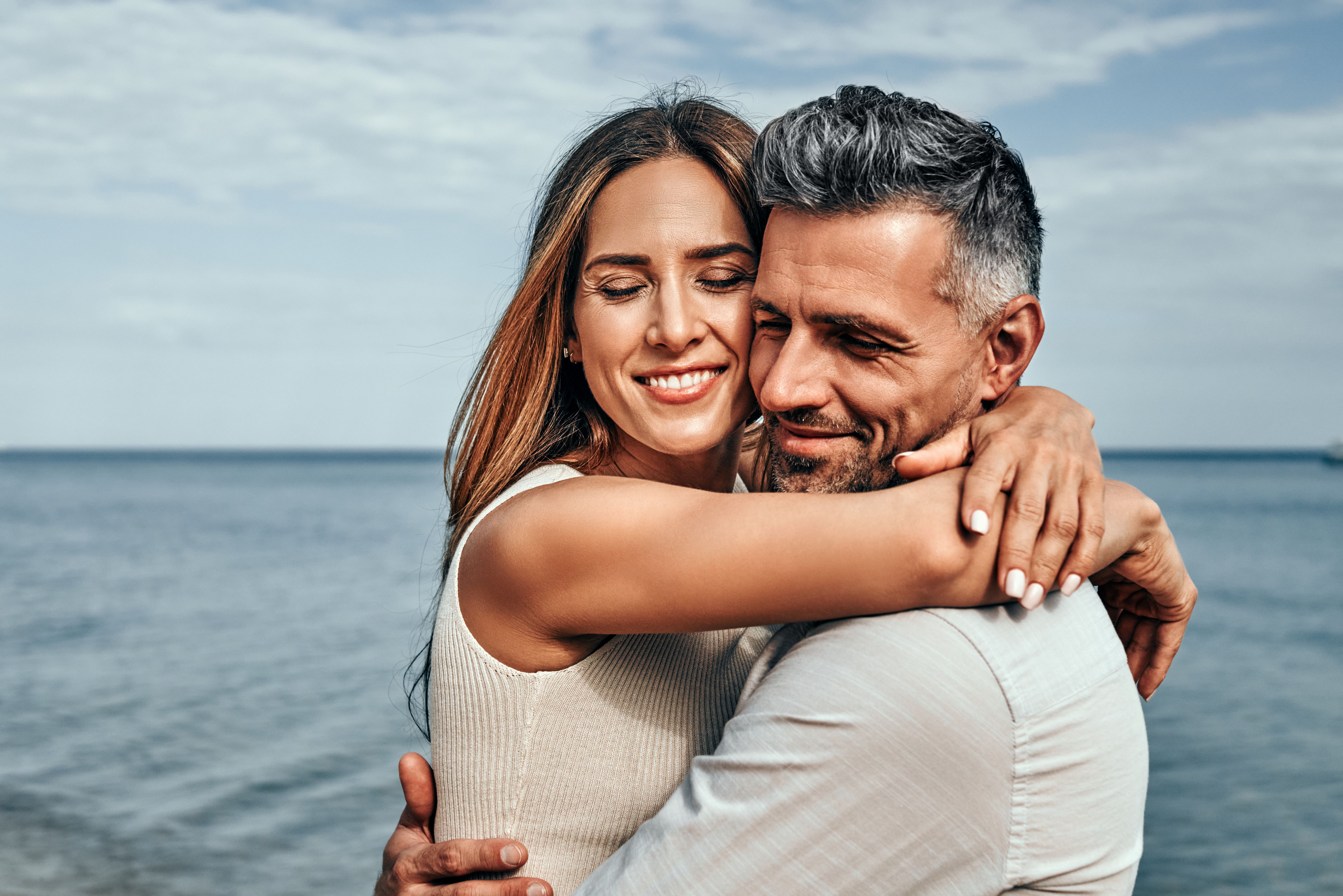 Couple d’une quarantaine d’années enlacé sur une plage estivale, illustrant une rencontre sérieuse, une relation durable et la confiance au sein du couple.