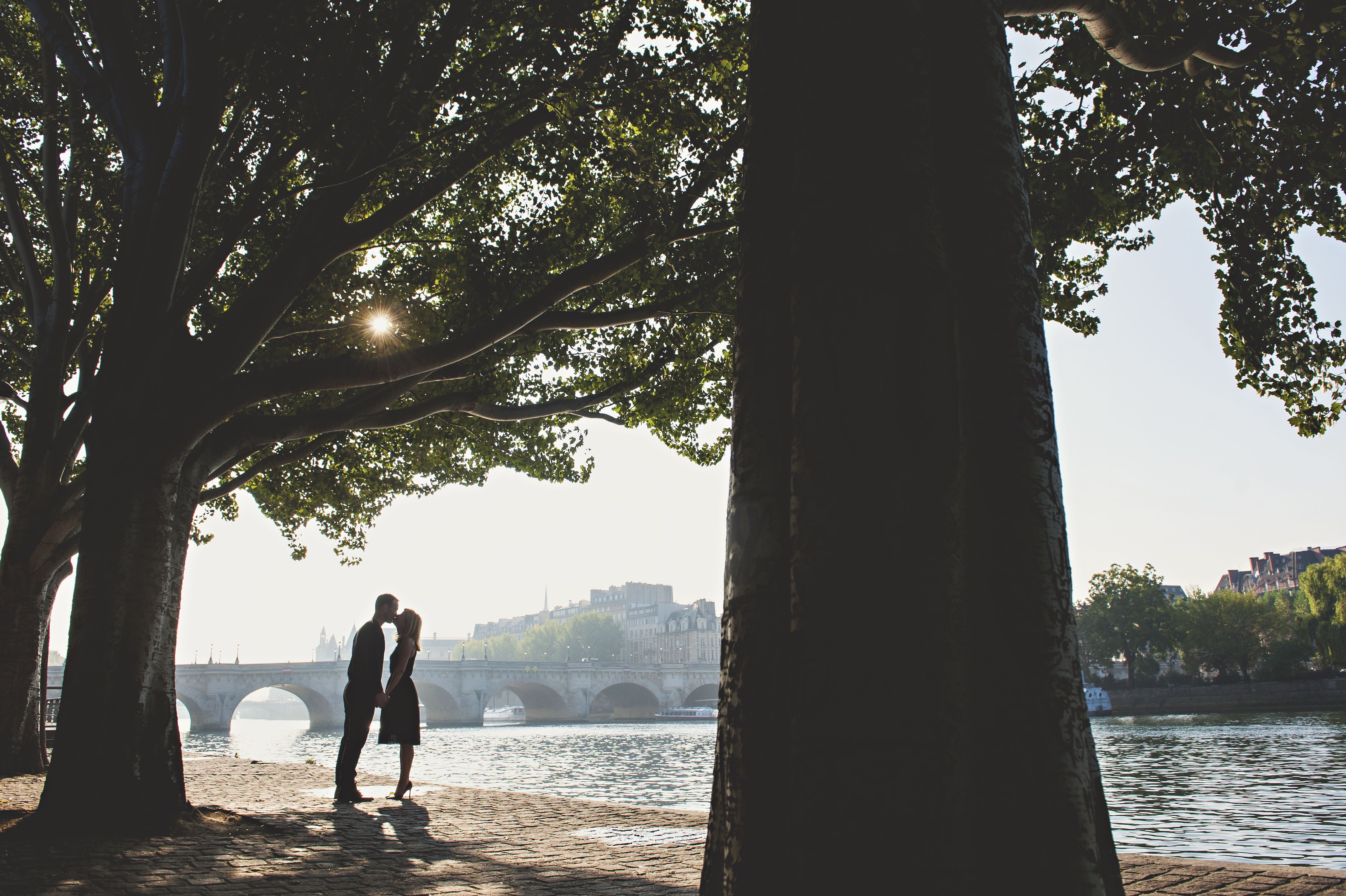 Couple s’embrassant au bord d’un lac devant un vieux pont en pierre, illustrant une rencontre sérieuse, une relation durable et des instants de complicité.