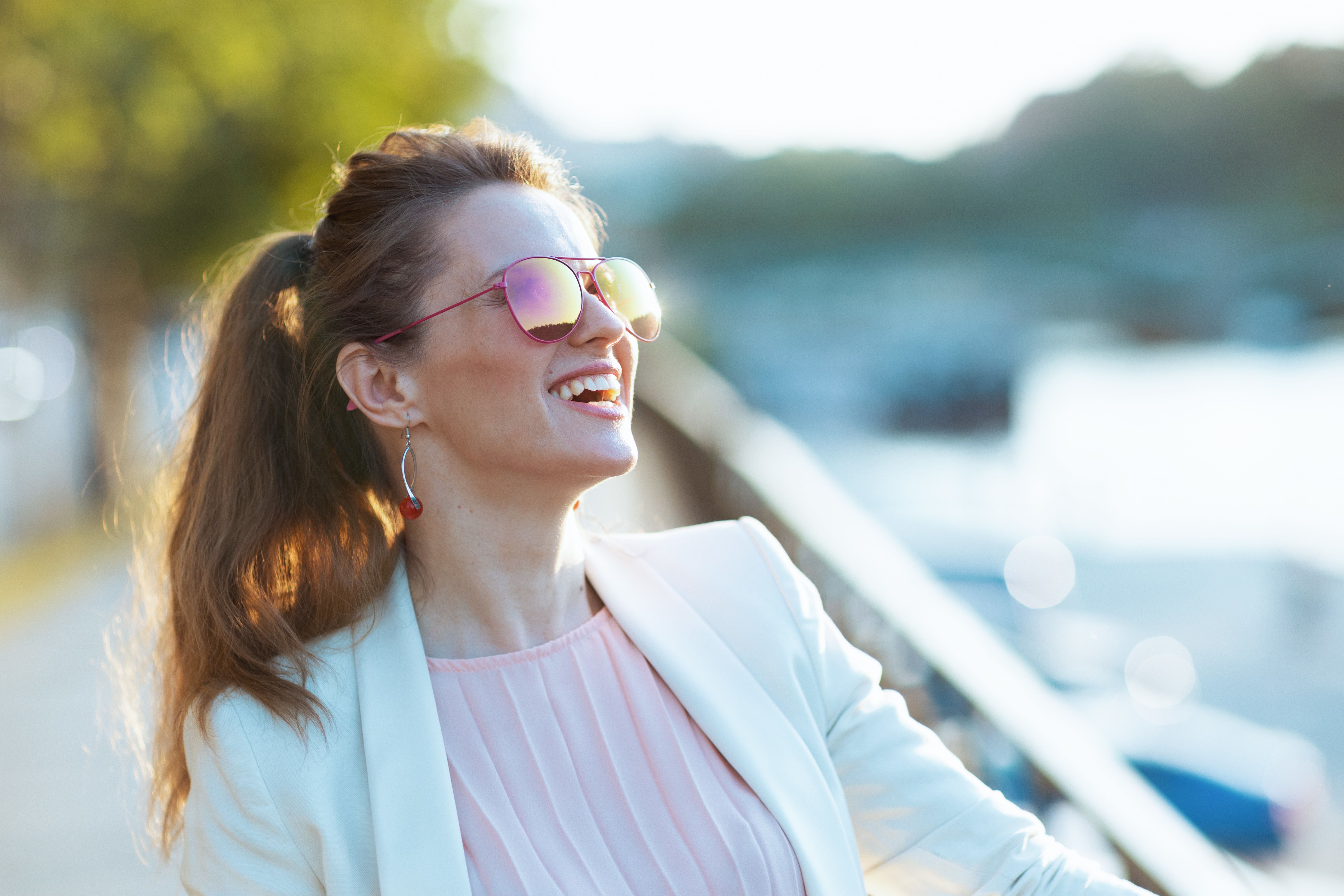 Jeune femme souriante avec des lunettes de soleil, assise à la terrasse en attendant son premier rendez-vous après une rencontre sur un site de rencontre sérieux.